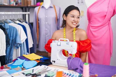 İspanyol kadın terzisi dikiş makinesi kullanıyor. Yüzünde gülümseme ve doğal ifadeyle yan yana bakıyor. Kendinden emin gülen. 