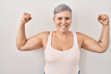 Middle age caucasian woman standing over white background showing arms muscles smiling proud. fitness concept. 