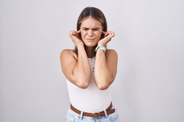 Beyaz arka planda duran Latin kökenli genç bir kadın yüksek sesli müzik sesi için parmaklarıyla kulaklarını kapatıyor. sağır kavramı. 