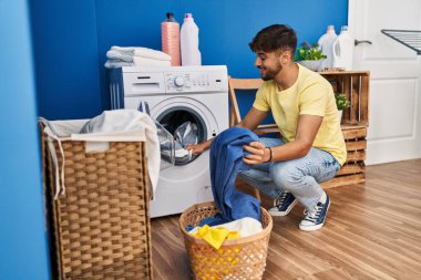 Genç Arap adam gülümsüyor çamaşırhanede çamaşır yıkayacak kadar kendinden emin.