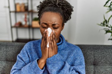 Afro-Amerikalı kadın evdeki kanepede peçete kullanıyor.