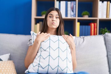 Kanepede oturan esmer kadın komik suratıyla yanaklarını şişiriyor. Ağzı havayla şişer, havayı yakalar.. 