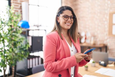 Ofiste akıllı telefon kullanan genç İspanyol iş kadını.