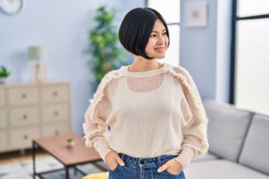 Genç Çinli kadın gülümsüyor. Evde kendinden emin duruyor.