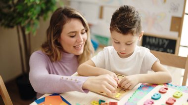 Anaokulunda masada oturan kadın ve çocuk matematik bulmaca oyunu oynuyorlar.