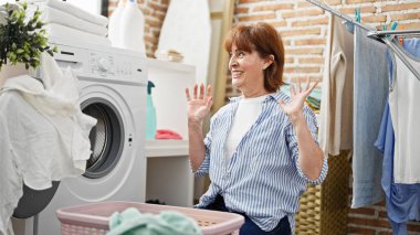 Middle age woman smiling confident washing clothes at laundry room