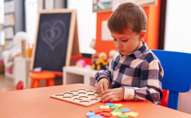 Anaokulunda masada oturmuş matematik oyunu oynayan sevimli beyaz çocuk.