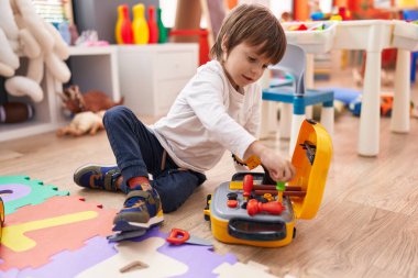 Sevimli beyaz çocuk anaokulunda yerde oturan aletlerle oynuyor.
