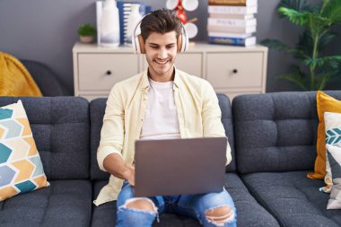 Genç İspanyol adam evdeki kanepede oturmuş müzik dinliyor.