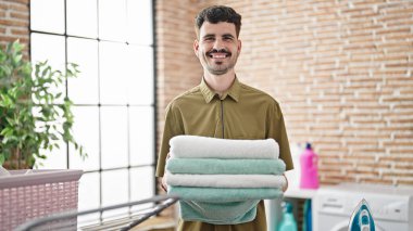 Çamaşır odasında katlanmış havluları tutan kendine güvenen İspanyol genç adam.