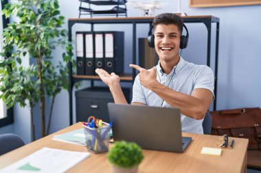 Ofiste çalışan genç İspanyol adam kulaklık takıyor kameraya hayret ediyor ve gülümsüyor.. 