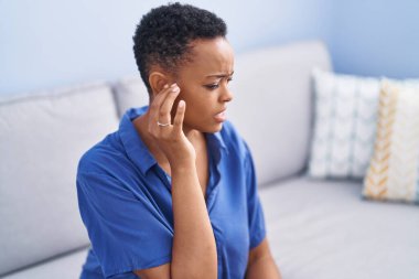 Afro-Amerikalı kadın kulak ağrısı çekiyor. Evdeki kanepede oturuyor.