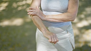 Middle age woman scratching arm at park clipart