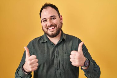 Ayrıca sarı arka plan başarısı tabelasının üzerinde duran sakallı, elinde olumlu bir jest yapan gülümseyen ve mutlu bir İspanyol. Neşeli ifade ve kazanan jest. 