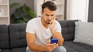 Evdeki kanepede oturan, akıllı telefon kullanan genç bir İspanyol.