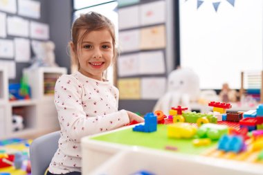 Anaokulundaki masada oturan, inşaat bloklarıyla oynayan sevimli İspanyol kız.