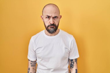 Young hispanic man with tattoos standing over yellow background depressed and worry for distress, crying angry and afraid. sad expression. 