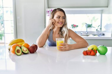 Young woman smiling confident holding orange juice at kitchen