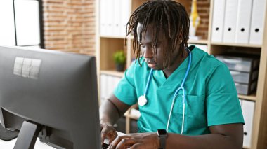 Afrikalı Amerikalı doktor klinikte bilgisayar kullanıyor.