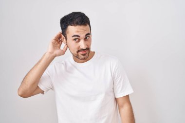 Beyaz arka planda dikilen yakışıklı İspanyol adam. Kulağından kulağa gülümsüyor. Dedikoduları ve dedikoduları dinliyor. Sağırlık kavramı. 