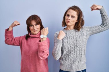 Mavi arka planda duran anne ve kızı gururla gülümseyen kol kaslarını gösteriyor. fitness konsepti. 