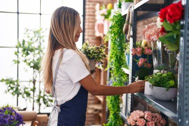 Young blonde woman florist holding plant at florist