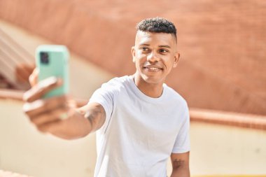 Young latin man smiling confident making selfie by the smartphone at street