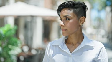 Young beautiful hispanic woman looking to the side with serious expression at coffee shop terrace
