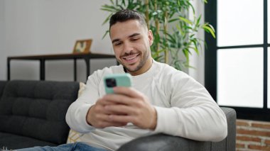 Evdeki kanepede oturan, akıllı telefon kullanan genç bir İspanyol.