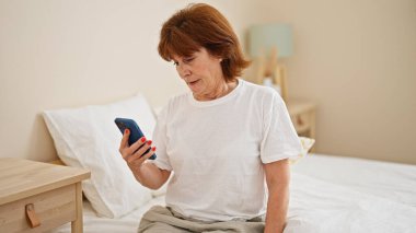 Orta yaşlı bir kadın yatakta akıllı telefon kullanıyor.
