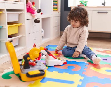 Anaokulunda yerde oturmuş süpermarket oyunu oynayan sevimli İspanyol çocuk.