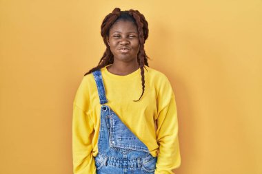 African woman standing over yellow background puffing cheeks with funny face. mouth inflated with air, crazy expression. 