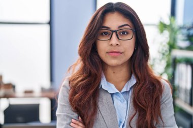 Genç İspanyol kadın iş işçisi ofiste kollarını kavuşturup el kol hareketi yapıyor.