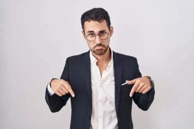 Beyaz arka plan üzerinde duran yakışıklı İspanyol adam üzgün ve üzgün görünüyor, parmaklarıyla yönü gösteriyor, mutsuz ve depresif.. 