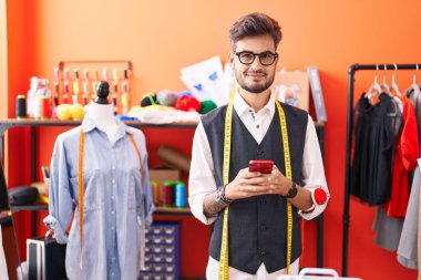 Genç İspanyol terzi atölyedeki akıllı telefonu kullanarak gülümsüyor.