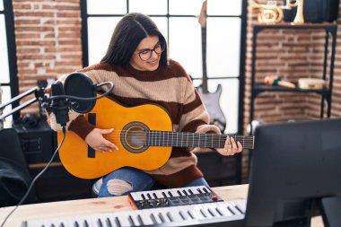 Young hispanic woman musician playing spanish guitar at music studio