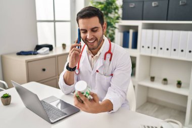 Doktor üniforması giyen genç İspanyol adam klinikte akıllı telefonla ilaç yazıyor.