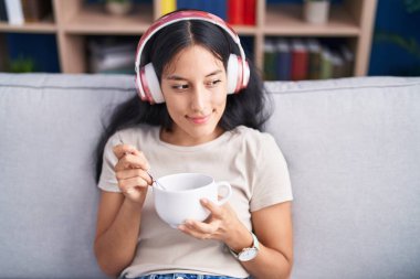 Young beautiful hispanic woman listening to music eating chinese food at home