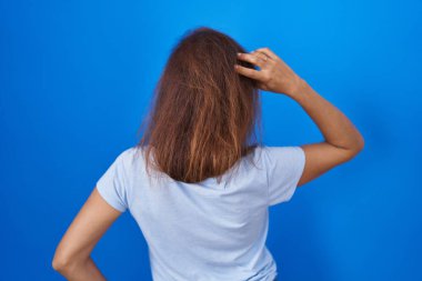 Esmer kadın mavi arka planda geriye doğru duruyor. Elleri başının üstünde şüpheyi düşünüyor. 