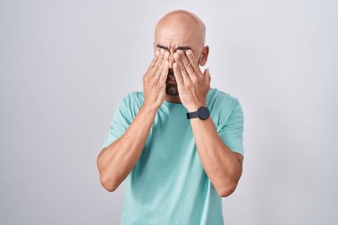 Orta yaşlı kel bir adam beyaz arka planda duruyor. Yorgunluk ve baş ağrısı için gözlerini ovuşturuyor. Uykulu ve yorgun bir ifade. görme sorunu 