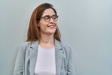 Gri arka planda duran esmer kadın yan tarafa bakıyor, rahat poz veriyor doğal yüzü ve kendine güvenen bir gülümsemesi var.. 