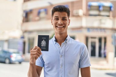 Young hispanic man smiling confident holding canada passport at street