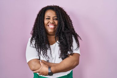 Ayrıca pembe arka planda durup kollarını kavuşturup kameraya gülümseyen İspanyol bir kadın. pozitif kişi. 