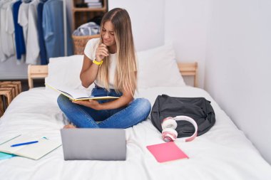Young beautiful hispanic woman student reading book studying on bed at bedroom