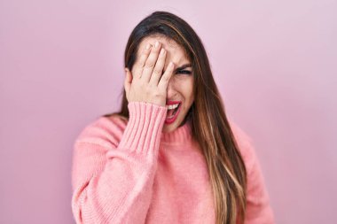 Young hispanic woman standing over pink background yawning tired covering half face, eye and mouth with hand. face hurts in pain. 