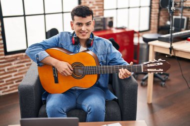 Young non binary man musician playing classical guitar at music studio
