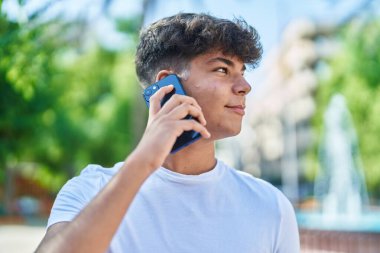 Genç İspanyol genç, gülümsüyor. Parktaki akıllı telefondan konuşuyor.