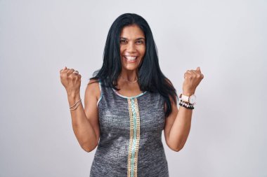 Beyaz arka planda dikilen olgun İspanyol kadın şaşkınlığı ve şaşkınlığı kollarını kaldırarak ve gözlerini açarak kutluyor. Kazanan konsept. 