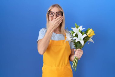 Çiçekçi önlüğü giymiş beyaz bir kadın çiçekleri tutarken ağzı yanlışlıkla ellerle kapatırken şok olmuş. gizli kavram. 