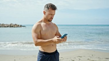 Kumsalda akıllı telefon kullanan genç bir turist.